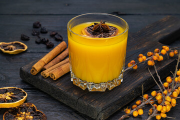 A glass of yellow juice. fresh sea buckthorn berries on the board.