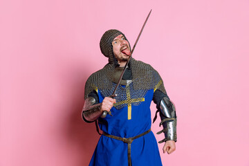 Portrait of man, medieval warrior or knight in armor with sword isolated over pink studio background