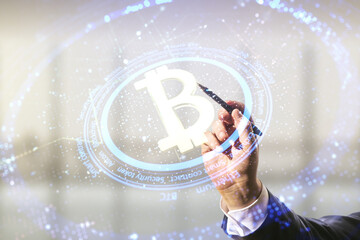 Double exposure of male hand with pen working with creative Bitcoin symbol hologram on blurred office background. Mining and blockchain concept