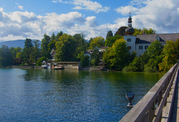 Fototapeta na wymiar background view of the outskirts of the island with the Orth castle and the central tower from the middle of the wooden bridge, in the middle of the Traunsee lake, Gmunden, Salzkammergut, Austria