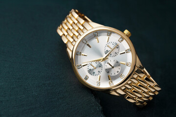 A gold wristwatch with a white dial rests on a stone table.