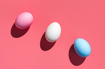Three Easter eggs of different colors on a pink background.