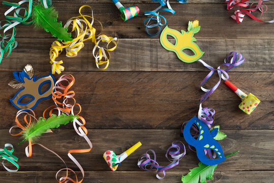 Carnival decoration on rustic wooden background with copy space in the center. Masks with ribbons and other carnival elements.