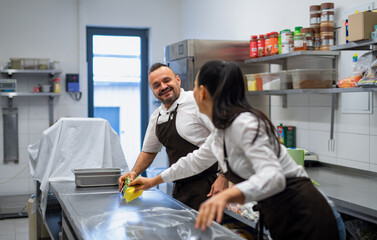 Naklejka premium Chef and cook cleaning the workspace after doing dishes indoors in restaurant kitchen.