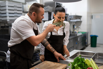 Chef giving herbs to smell to his colleague in commercial kitchen.
