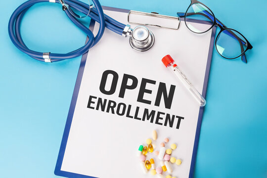 OPEN ENROLLMENT. Stethoscope and paper plate with a sheet of white paper with text OPEN ENROLLMENT blue backround. Medical concept