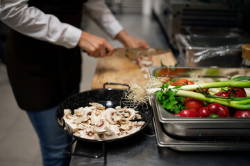 Close-up of unrecognizable chef cutting mushrooms indoors in restaurant kitchen.