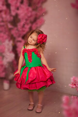 charming little girl brunette in a rose dress on March 8 on a floral background poses in spring
