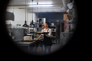 Happy chef and cook working on their dishes in restaurant kitchen, shot through circle door window.