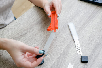 A woman changes a blade in a mounting knife. Hands hold the knife and the new sharp blade. Selective focus. Red plastic knife.