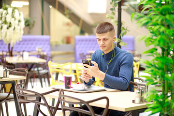 Young man works online. In the hands of a smartphone, gadgets for working on the Internet. A man in a cafe reads the news and works using the phone.
