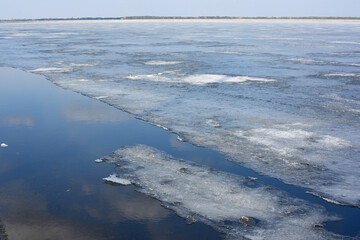 Winter landscape with partly frozen river. Ice floes float on the blue surface. Ice drift. Global...