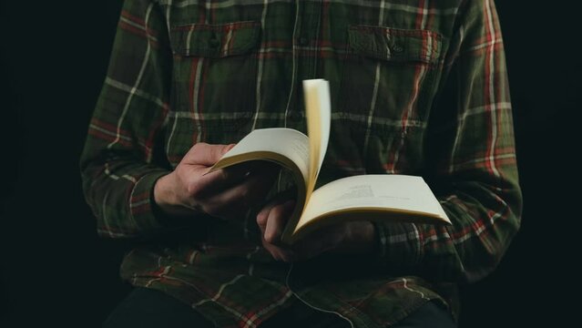 Close up video of man flip through a book over dark background.