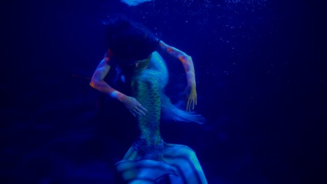 enigmatic mermaid with big tail is floating in blue depth of ocean, fascinating underwater shot