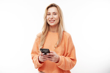 Beautiful blonde girl in casual looks at the smartphone screen and smiles isolated on white studio background