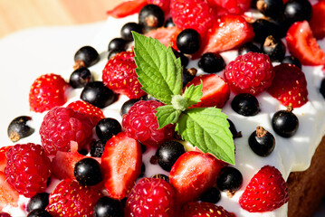 Fototapeta na wymiar raspberries, currants, strawberries, cherries, mint with whipped cream, berry background