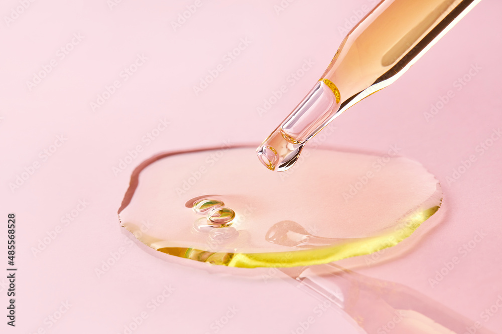 Wall mural close up of pipette with pouring liquid essential oil on pink background. dropper with a falling dro