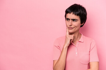 Young caucasian woman isolated on pink background looking sideways with doubtful and skeptical expression.