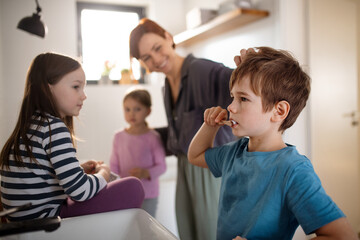 Mother with three little children in bathroom, brushing teeth.