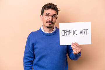 Young caucasian man holding a crypto art placard isolated on beige background dreaming of achieving goals and purposes