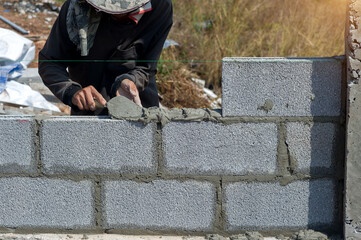 masonry worker make concrete wall by cement block and plaster at construction site