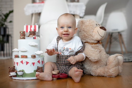 tiny adorable baby sit on floor near the birthday cake and teddy bear. Looking with sharp eyes. Close-up photo