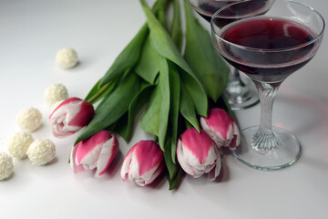 Spring holiday. Tulips, candies and glasses with wine on a white background.