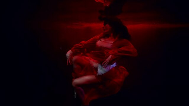 alluring lady in red dress is swimming alone in dark deepness with dramatic red light