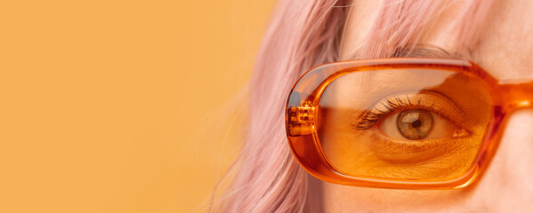 Beautiful young woman wearing cool orange sunglasses on yellow background. Close-up of woman eye