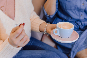 photo of young fascinating unrecognizable blond woman with cup of tea . Sitting on couch with friend and holding cup.