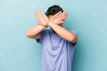 Young caucasian man isolated on blue background keeping two arms crossed, denial concept.