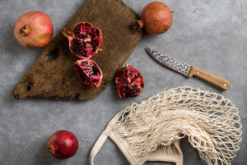 Beautiful red pomegranate fruit composition on a concrete background. Half pomegranate and ripe pomegranate fruit with rustic wooden board, knife and string bag. Top view. - 485572570