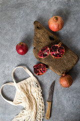 Beautiful red pomegranate fruit composition on a concrete background. Half pomegranate and ripe pomegranate fruit with rustic wooden board, knife and string bag. Top view. - 485572577
