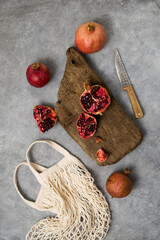 Beautiful red pomegranate fruit composition on a concrete background. Half pomegranate and ripe pomegranate fruit with rustic wooden board, knife and string bag. Top view. - 485572714