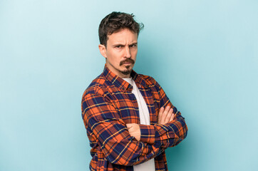 Young caucasian man isolated on blue background frowning face in displeasure, keeps arms folded.