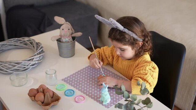 Adorable little girl with bunny ears headband coloring easter eggs. Decoration for Easter day as a tradition in spring.