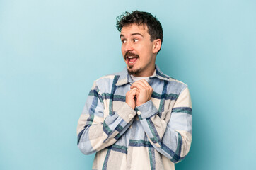 Young caucasian man isolated on blue background praying for luck, amazed and opening mouth looking to front.