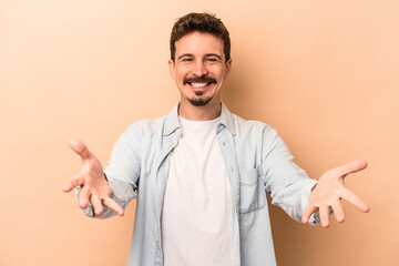 Young caucasian man isolated on beige background showing a welcome expression.