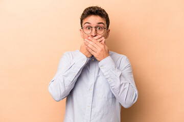 Young caucasian man isolated on beige background covering mouth with hands looking worried.