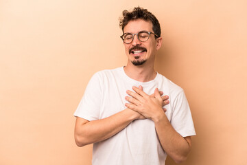 Young caucasian man isolated on beige background laughing keeping hands on heart, concept of happiness.