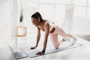 Fit young African American woman with earphones doing strength workout in front of laptop at home