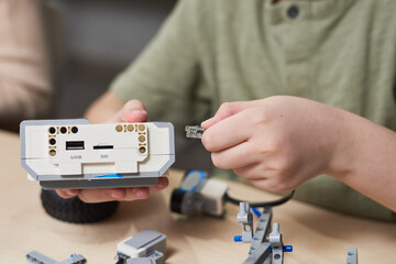 Close up of unrecognizable boy connecting cables to control module while building robot in...
