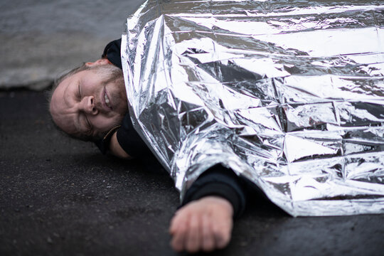 Unconscious man in medical shock lying under emergency blanket