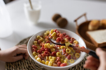 Cute little caucasian girl sitting at table on kitchen early morning and preparing breakfast with colorful cornflakes and milk. Kid enjoying life with healthful food, healthy lifestyle concept