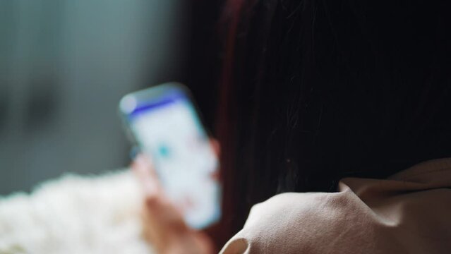 Online shopping concept. Young woman sitting on the bed and makes online shopping on a smartphone. Woman at Home Lying on Couch in Living Room Using Smartphone Buys in Internet Shop.
