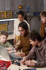 Vertical portrait of young male teacher with diverse group of children in robotics class at school