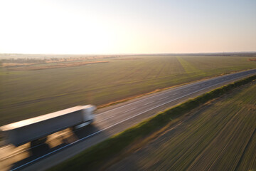 Aerial view of blurred fast moving semi-truck with cargo trailer driving on highway hauling goods in evening. Delivery transportation and logistics concept