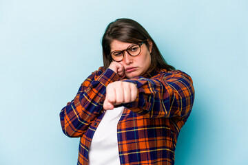 Young caucasian overweight woman isolated on blue background throwing a punch, anger, fighting due to an argument, boxing.