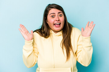 Young caucasian overweight woman isolated on blue background receiving a pleasant surprise, excited...