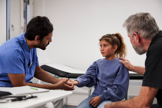 Male doctor examining girl patient's wrist during appointment